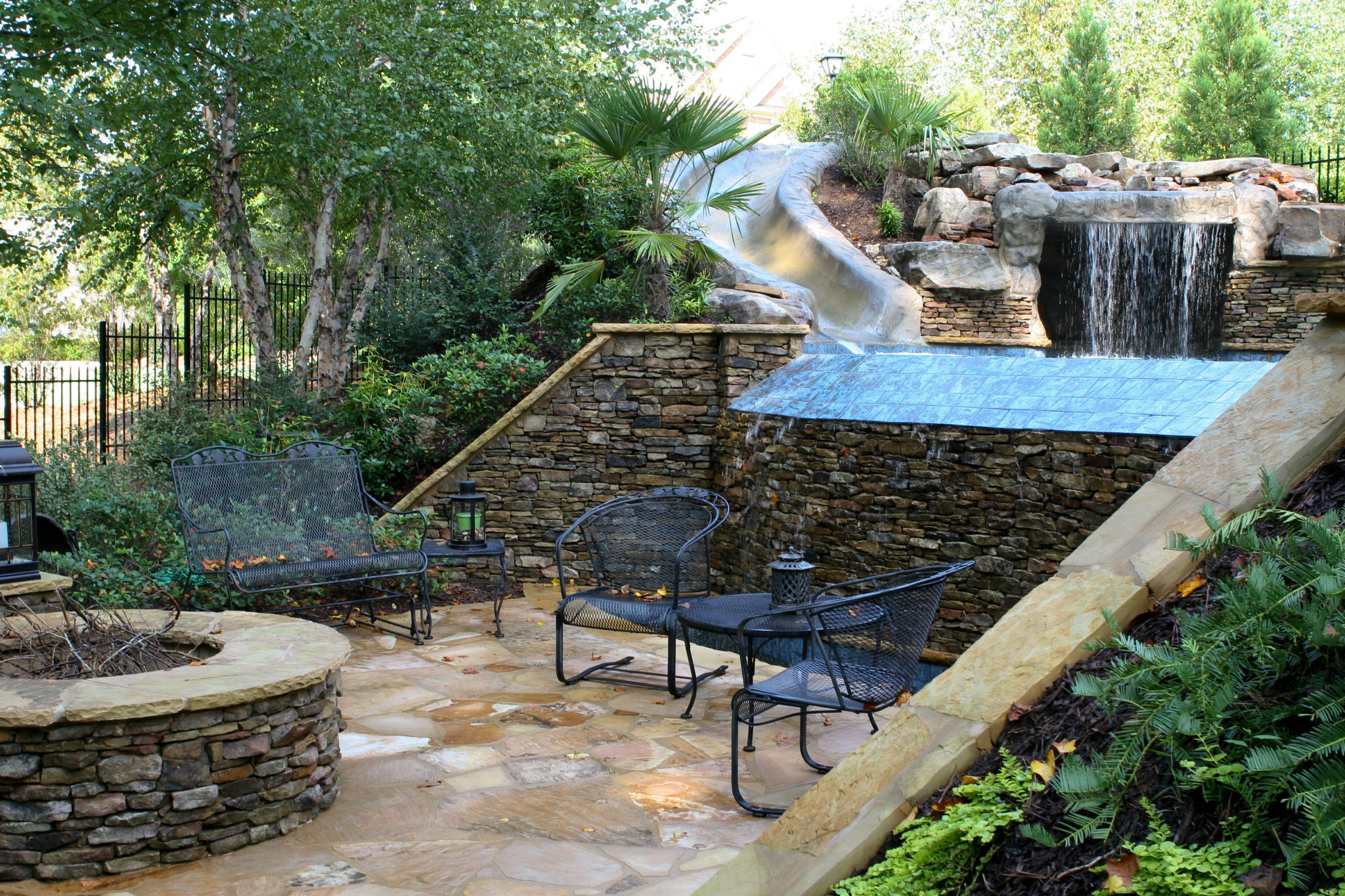 A stone vanishing edge pool with a waterslide and grotto nestled among lush greenery.