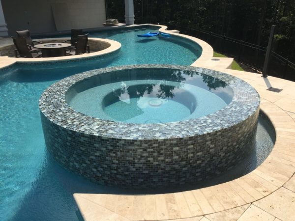 An elevated circular spa adorned with intricate multicolor tile, water cascading from all sides.