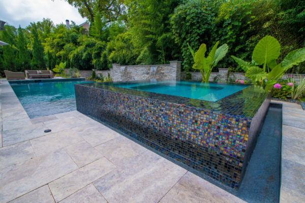 An elevated square spa adorned with intricate multicolor tile, water cascading from all sides.