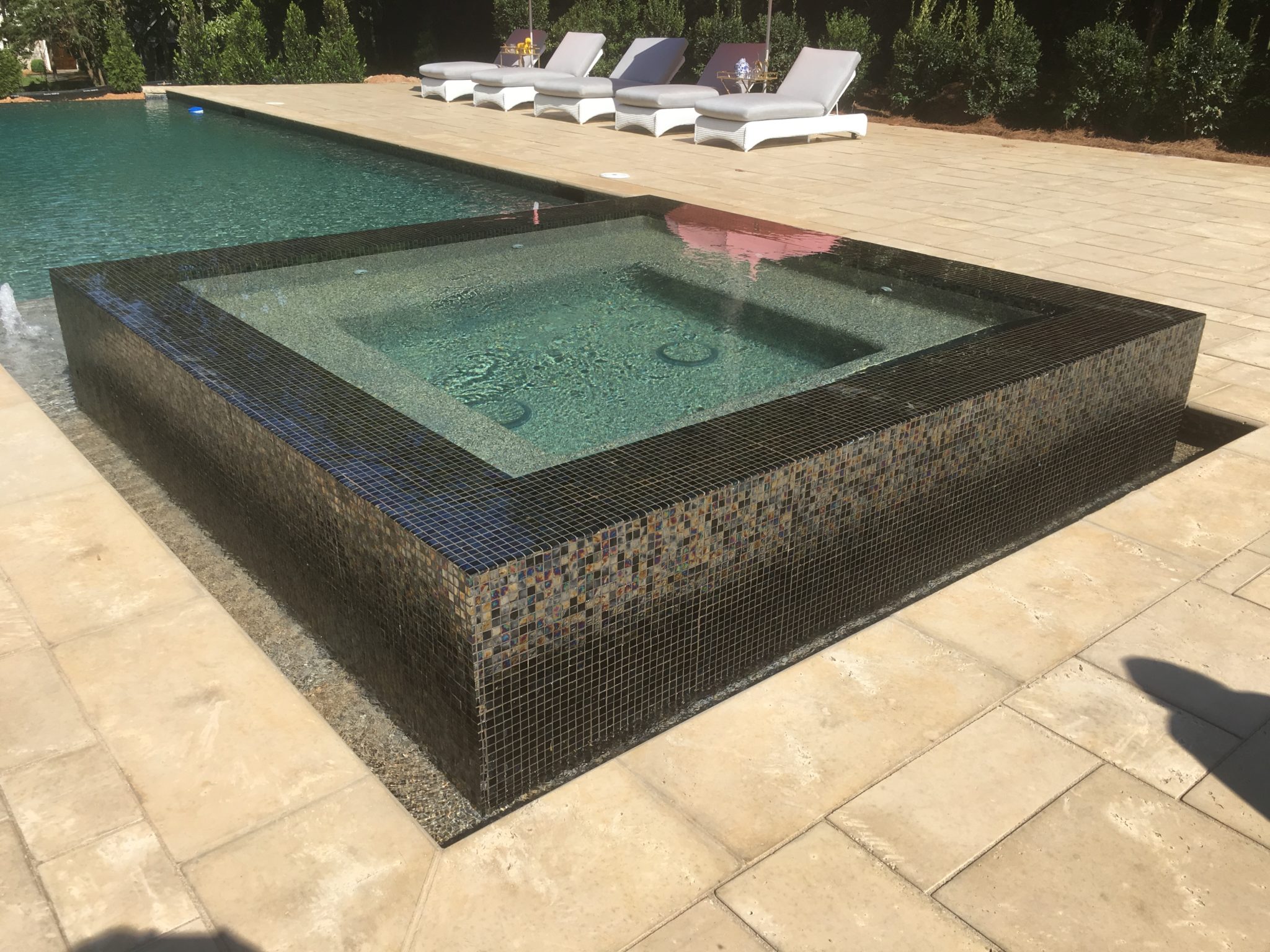 A raised square spa with vibrant custom multicolor tilework and water cascading over the edges.