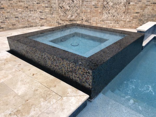 A raised square spa with vibrant custom multicolor tilework and water cascading over the edges.