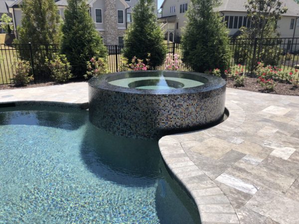 A raised circular spa with vibrant multicolor tilework and cascading water feature.