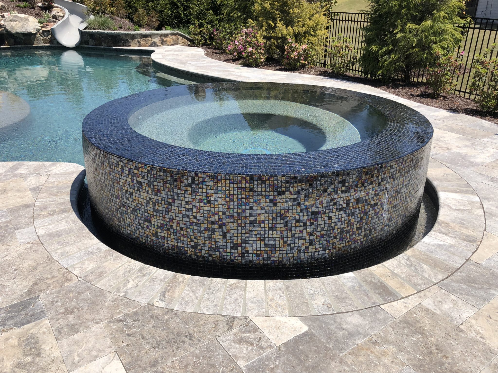 An elevated circular spa adorned with intricate multicolor tile, water cascading from all sides.