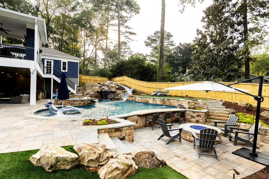 A custom freeform pool surrounded by lush greenery, with a boulder waterfall and slide.