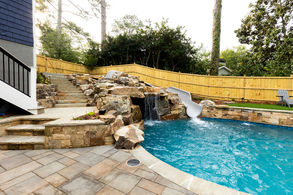 A picturesque boulder waterfall cascades into a pool with an adjacent waterslide.