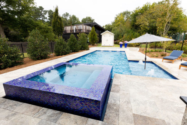 A raised square spa with tranquil custom blue tilework and water cascading over the edges.