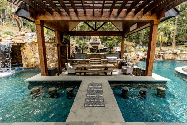 Expansive vanishing edge pool with a 360-degree spa, accompanied by a vast pergola, outdoor kitchen, lush artificial turf, and meticulously designed custom landscape