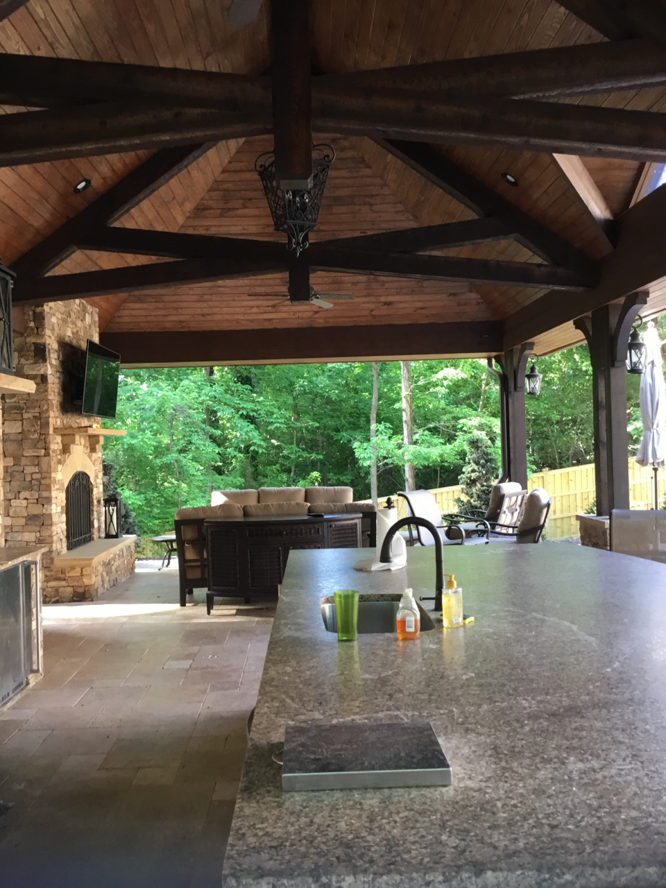 A picturesque vaulted cabana featuring a stone wall, fireplace, pizza oven, and fully equipped kitchen, adjacent to a luxurious swimming pool.
