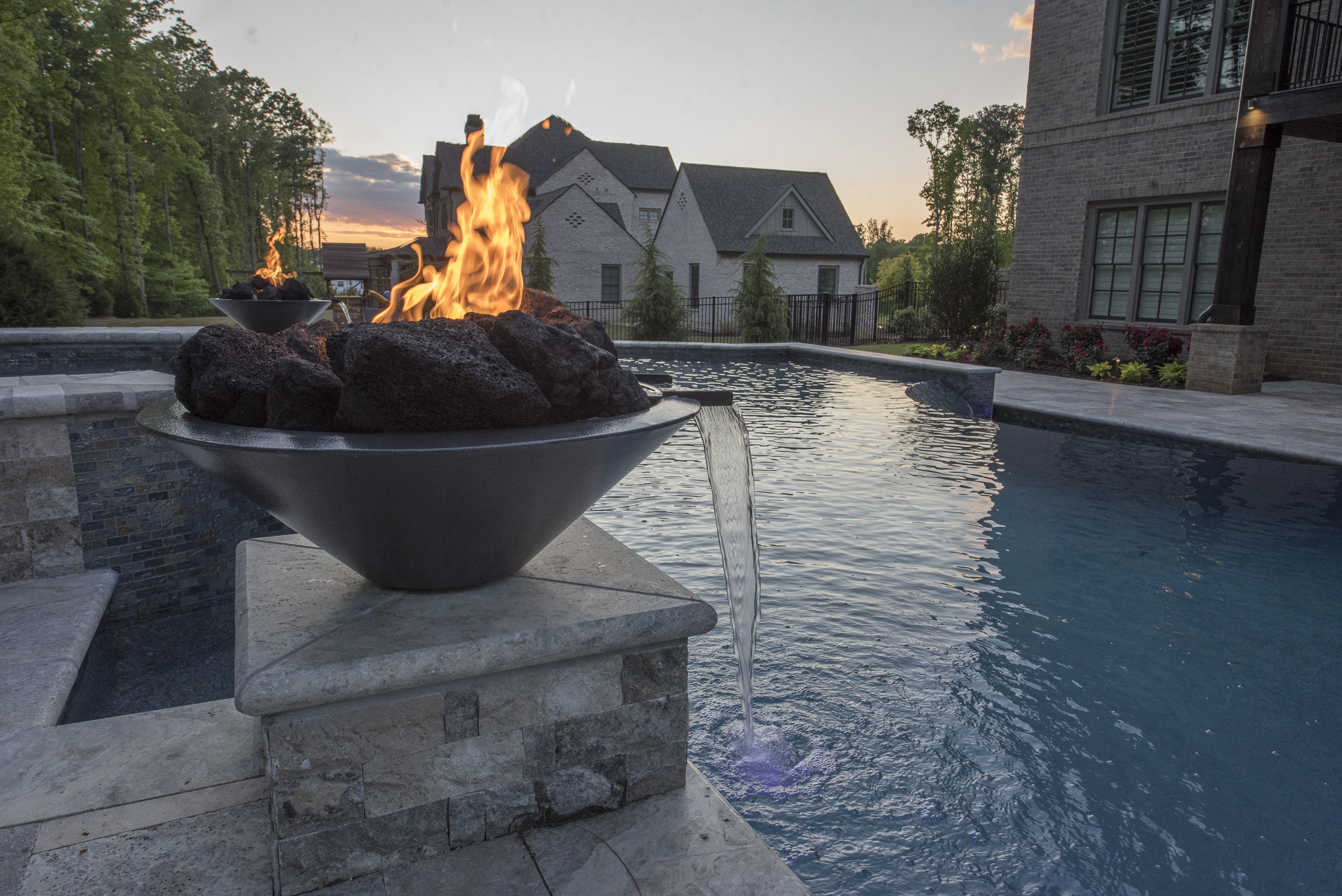A mesmerizing pool surrounded by stone columns adorned with fire bowls, casting a warm and enchanting glow over the tranquil waters.