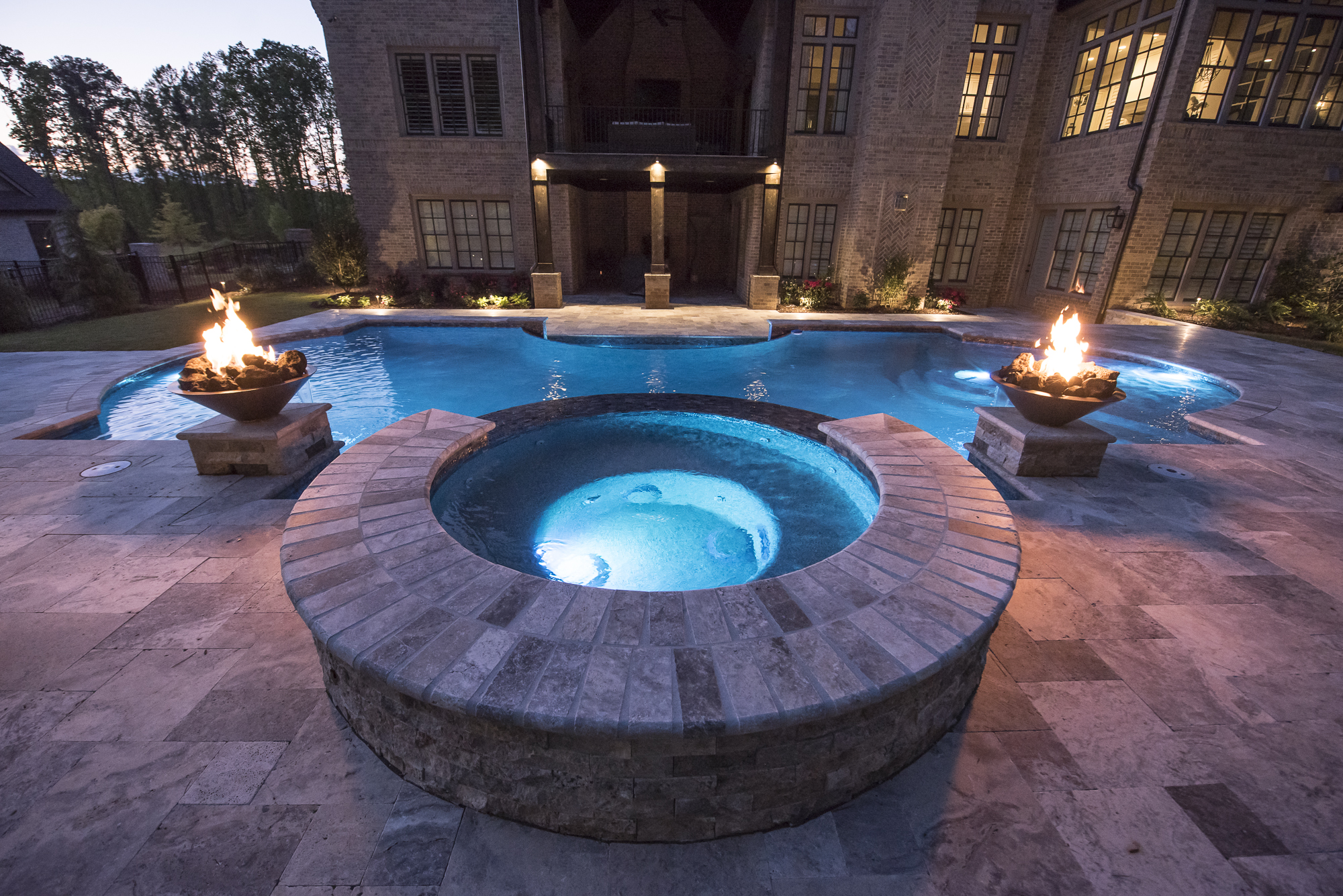 A mesmerizing pool surrounded by stone columns adorned with fire bowls, casting a warm and enchanting glow over the tranquil waters.