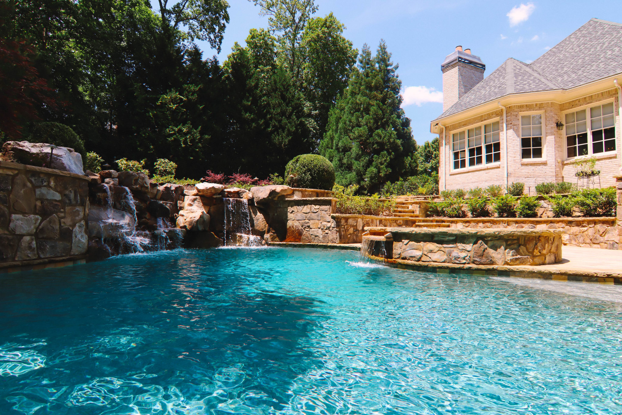 A picturesque boulder waterfall flowing into a pool surrounded by lush greenery.