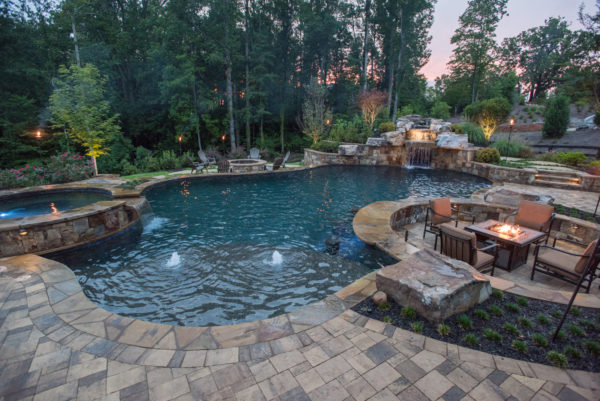 Aerial view of a custom freeform pool surrounded by lush greenery, with a boulder waterfall cascading into the pool and a sunken eating area.