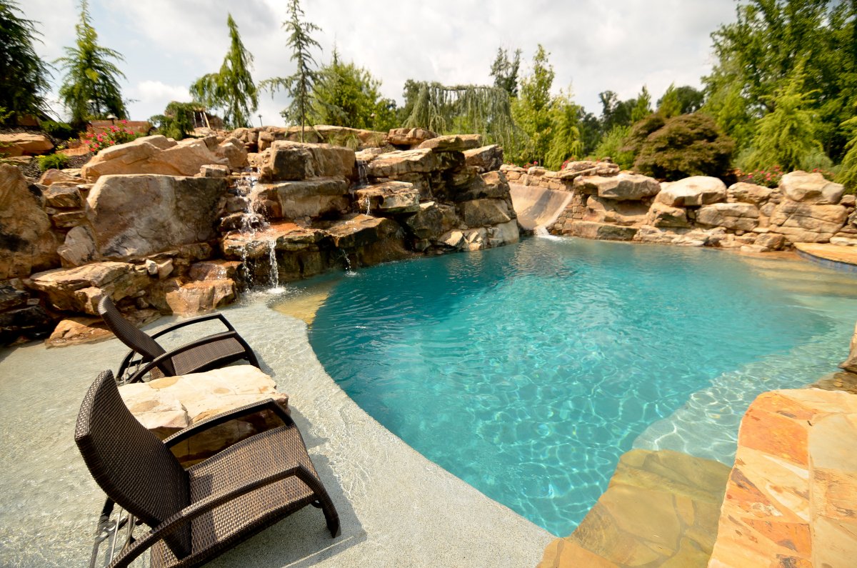 A custom freeform pool with a boulder waterfall and slide, surrounded by lush greenery.