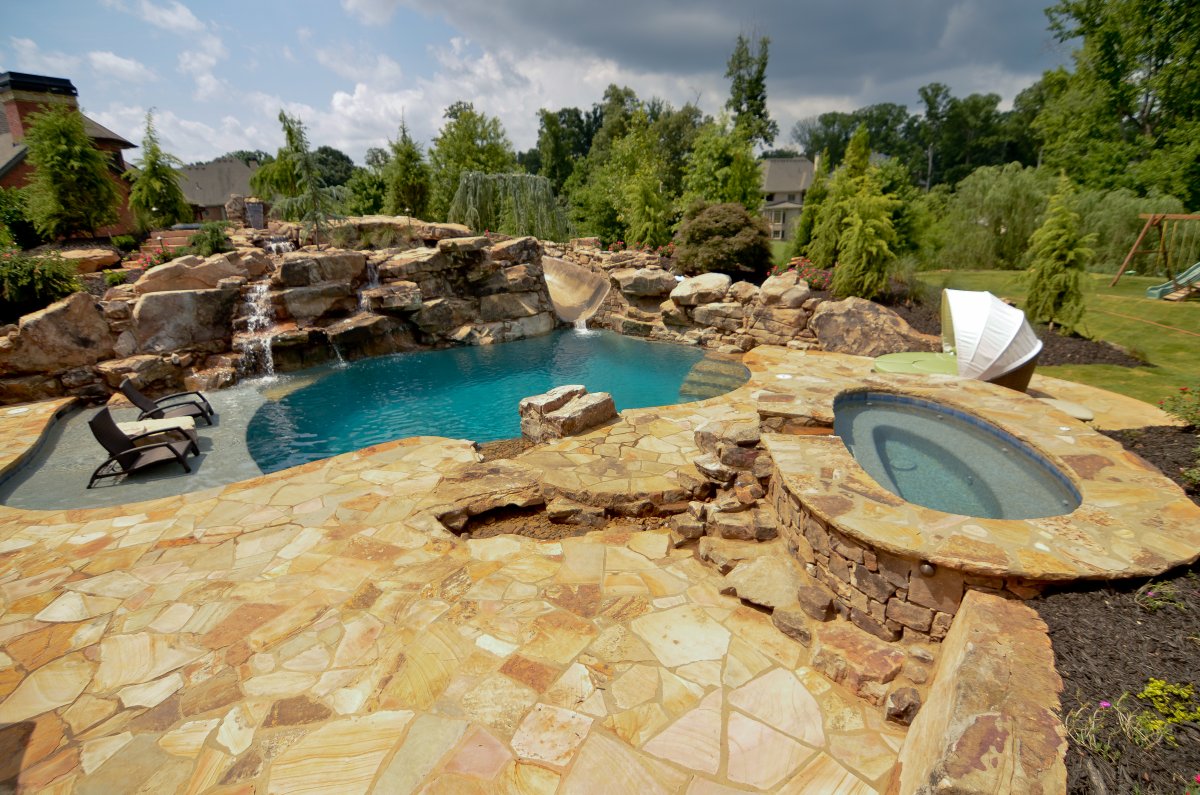 A custom freeform pool with a boulder waterfall and slide, surrounded by lush greenery.