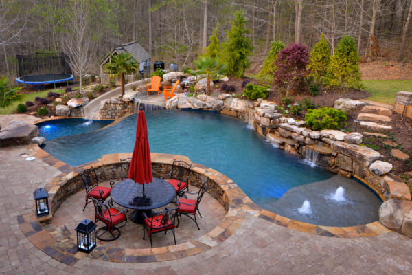 A custom freeform pool with a vanishing edge boulder waterfall overlooking lush greenery.