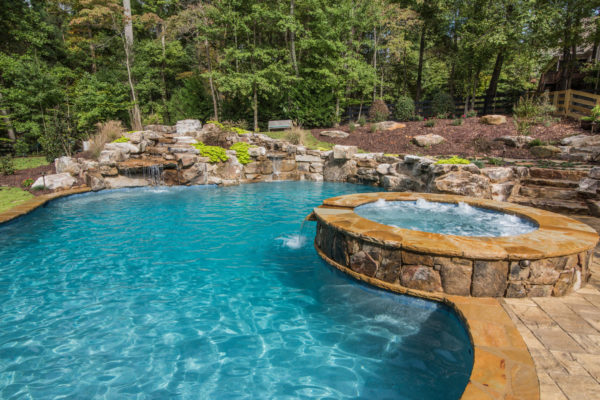 A custom freeform pool with a boulder waterfall surrounded by lush greenery.