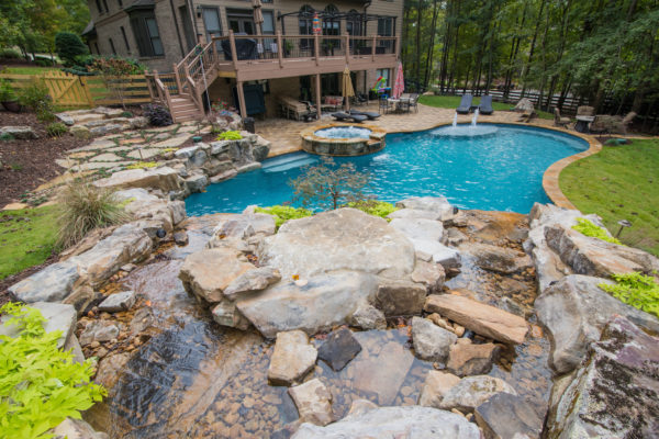 A custom freeform pool with a rustic boulder waterfall surrounded by lush greenery.