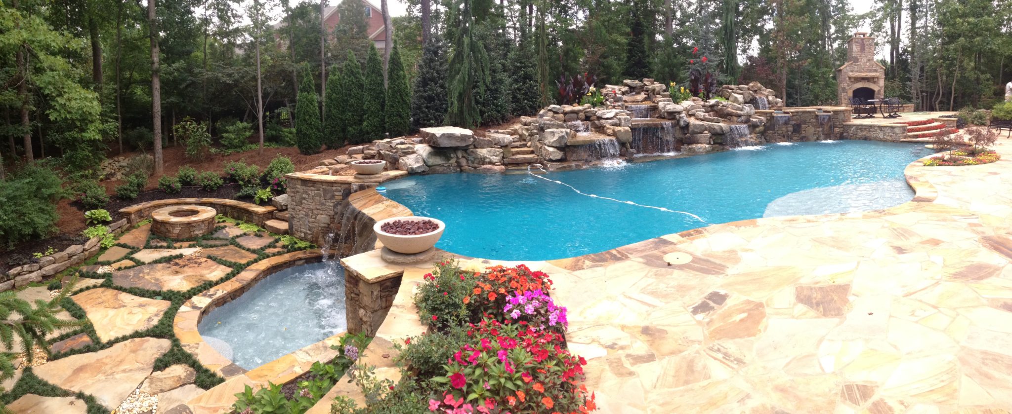 A picturesque custom freeform pool with a vanishing edge and fireplace overlooking lush landscape.
