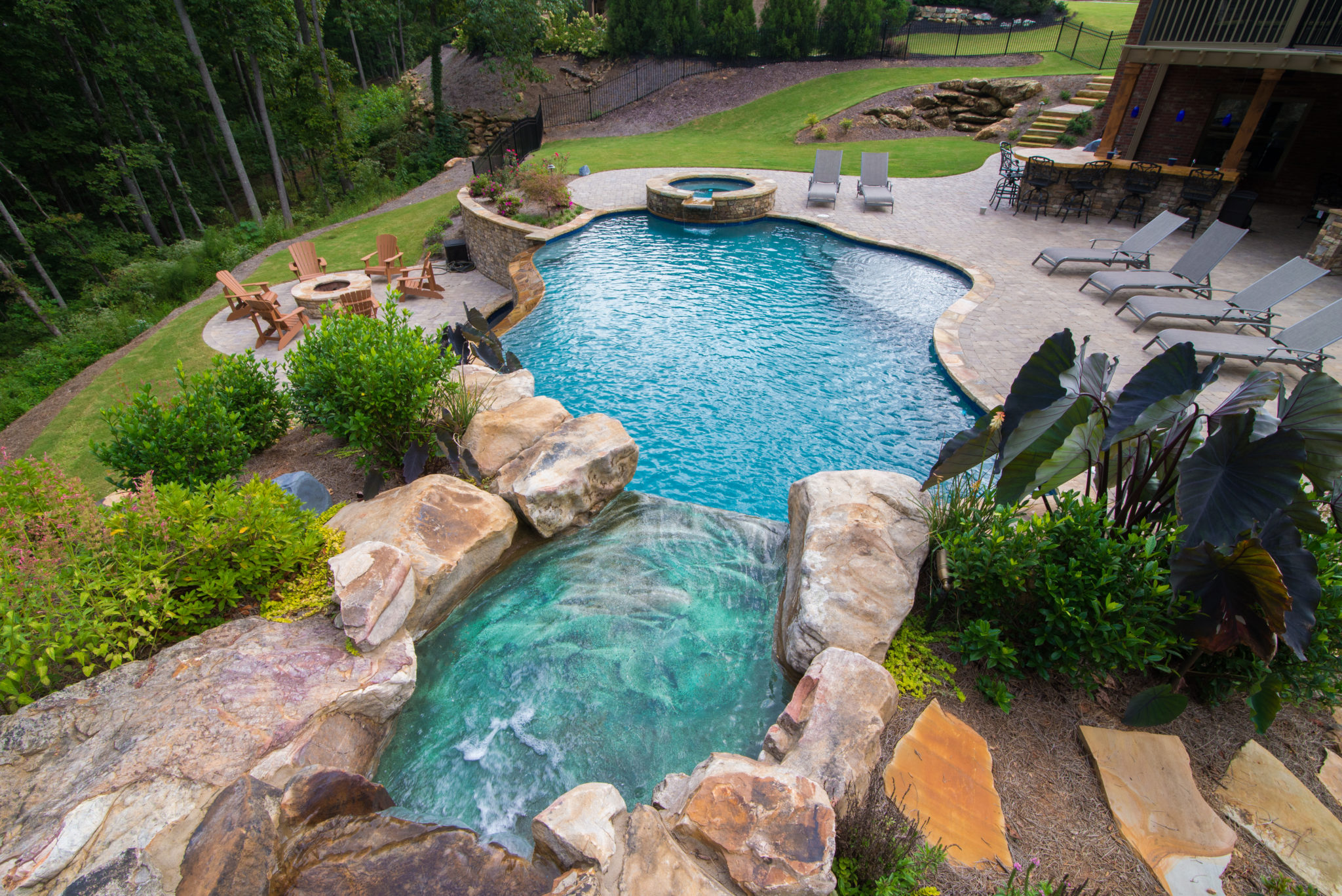A custom freeform pool with a boulder waterfall and grotto nestled in lush landscaping.
