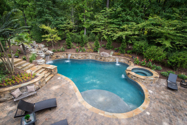 A picturesque view of a custom freeform pool with a boulder waterfall surrounded by lush greenery.