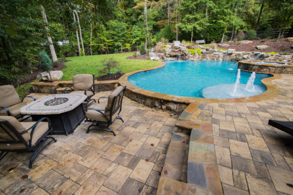A picturesque view of a custom freeform pool with a boulder waterfall surrounded by lush greenery.