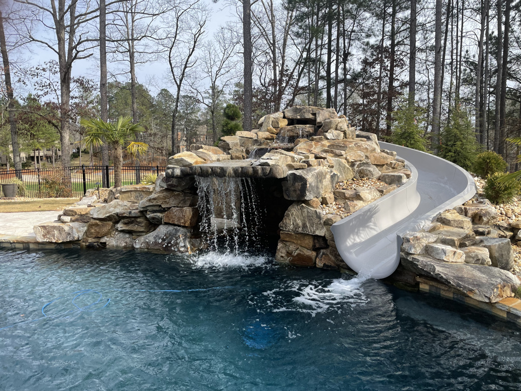 A stunning custom boulder waterfall grotto with a slide, surrounded by lush greenery.