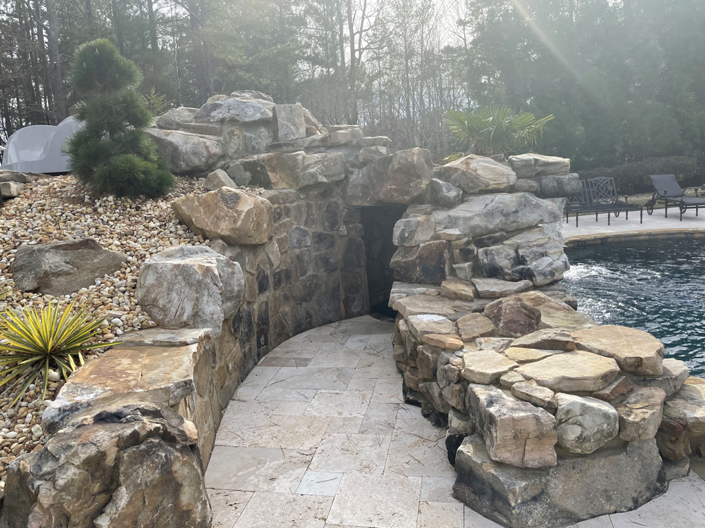 A custom boulder waterfall with slide and grotto, surrounded by lush vegetation, with a private entrance.