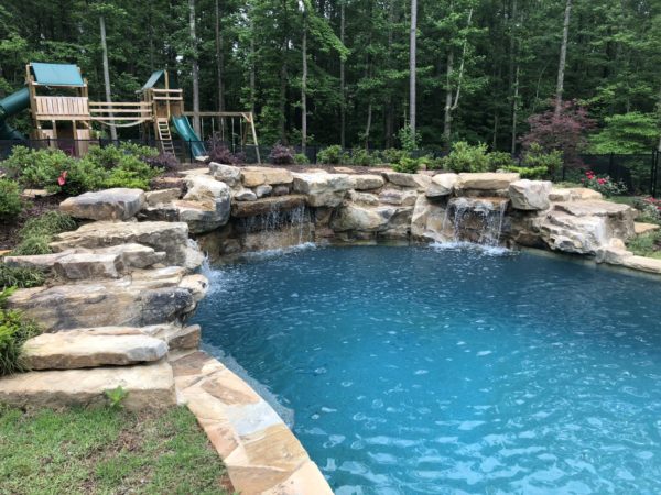 A custom boulder wall with multiple sheer descents pouring water into a swimming pool.
