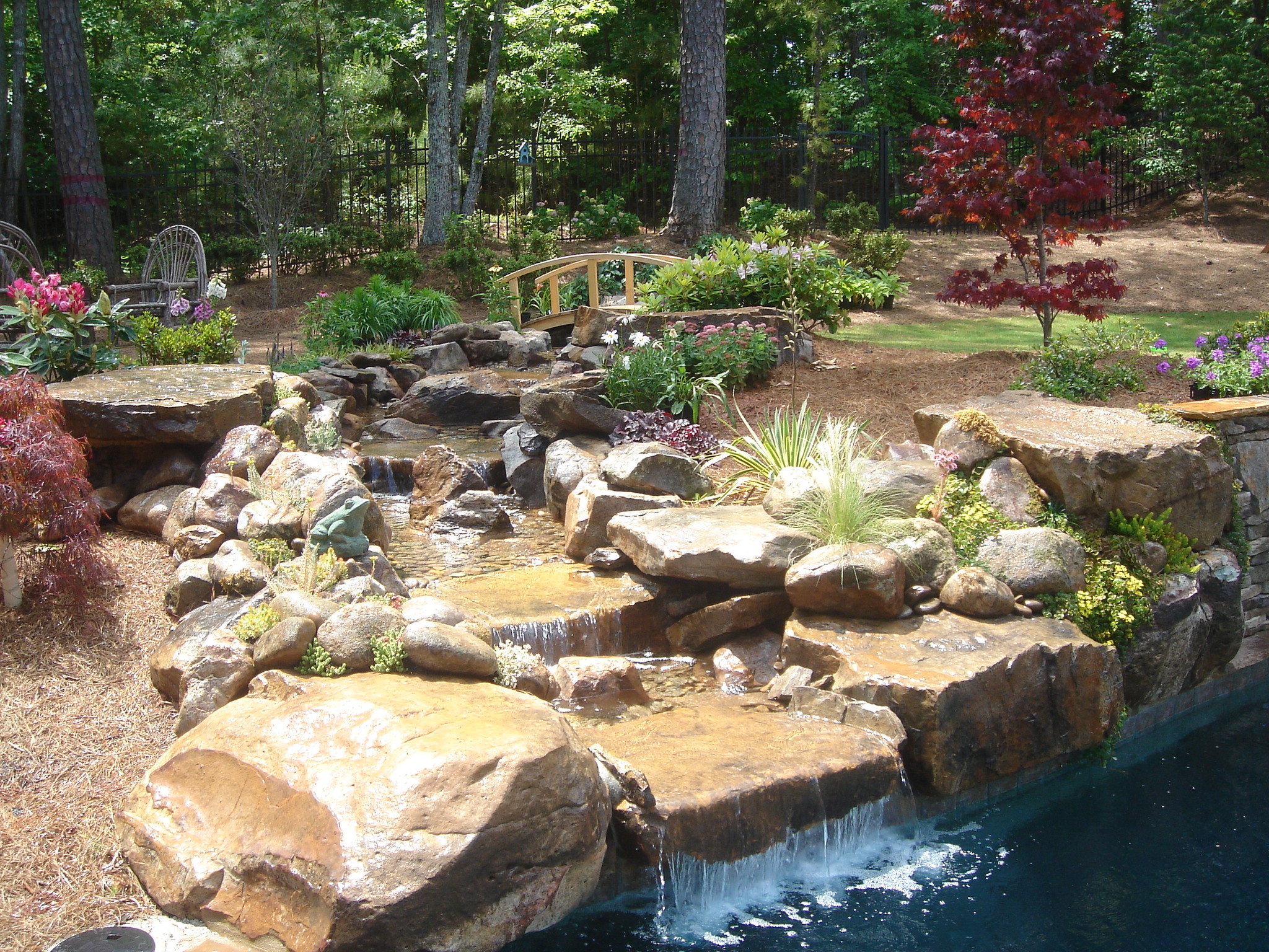 A stunning view of a custom three-tier boulder waterfall pool surrounded by lush greenery.