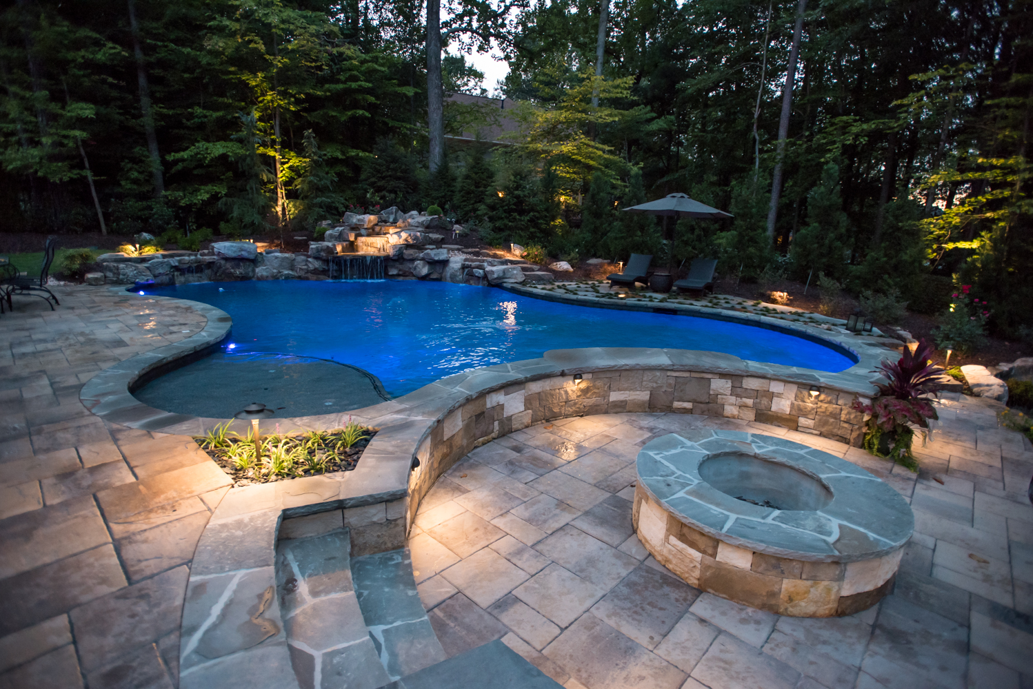 A breathtaking view of a custom two-tier boulder waterfall pool surrounded by lush landscaping.