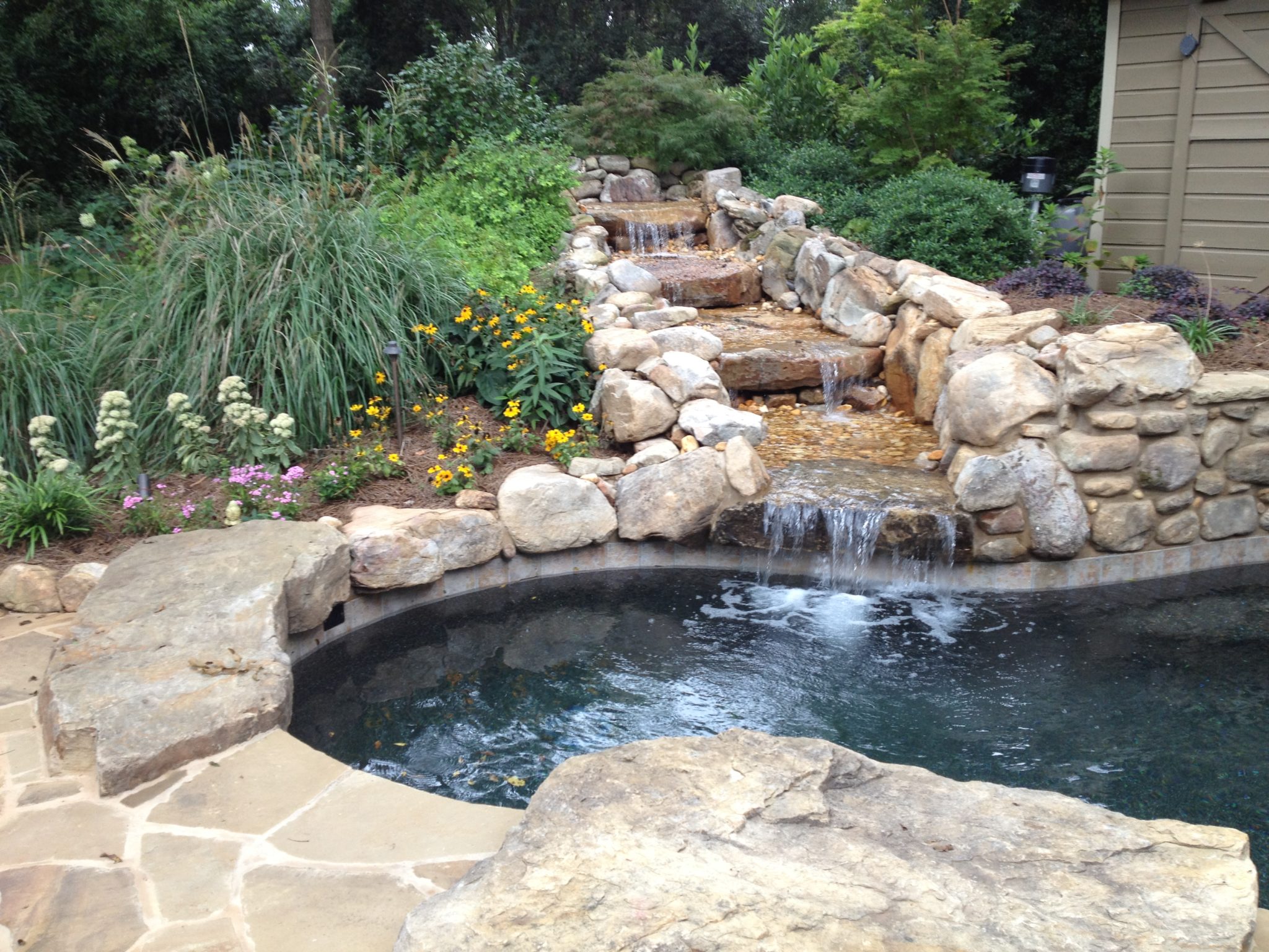 A custom four-tier boulder waterfall nestled in lush greenery.