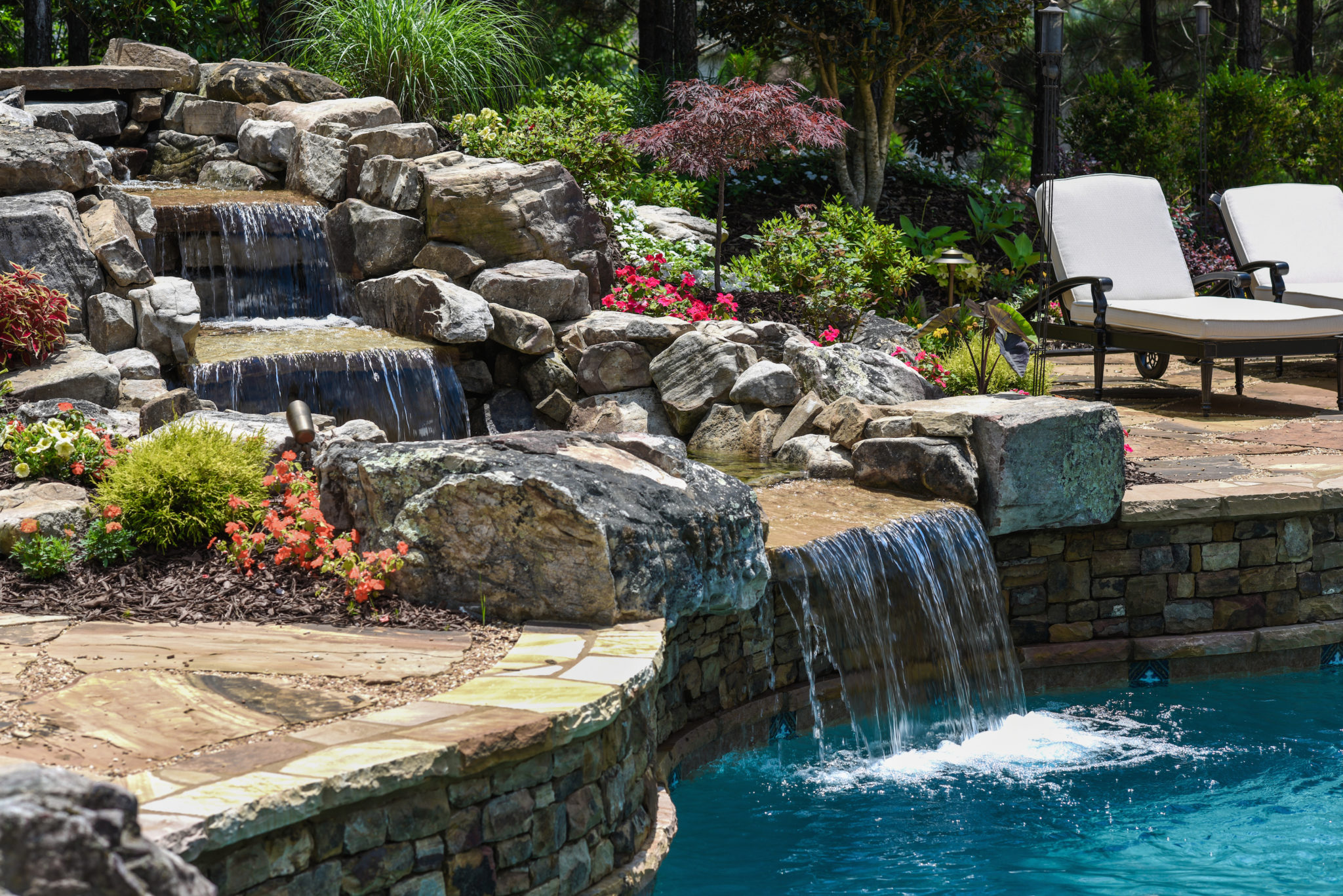 A custom three-tier boulder waterfall flowing into a swimming pool.