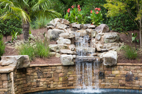 A custom three-tier boulder waterfall flowing into a swimming pool.