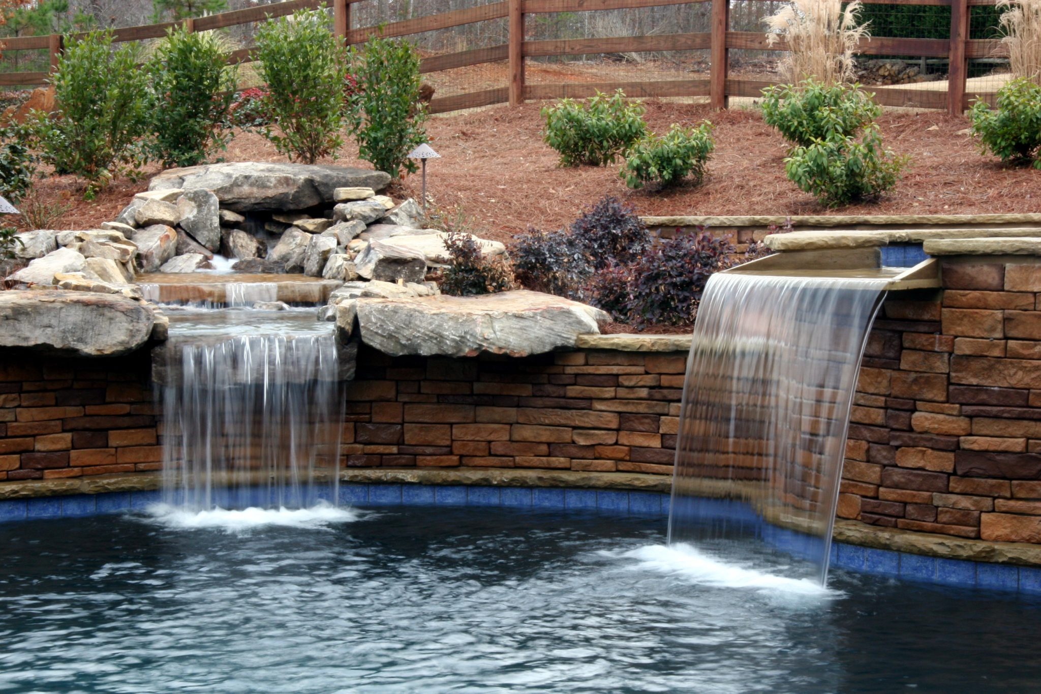 A custom boulder waterfall cascading into a spa in a swimming pool.