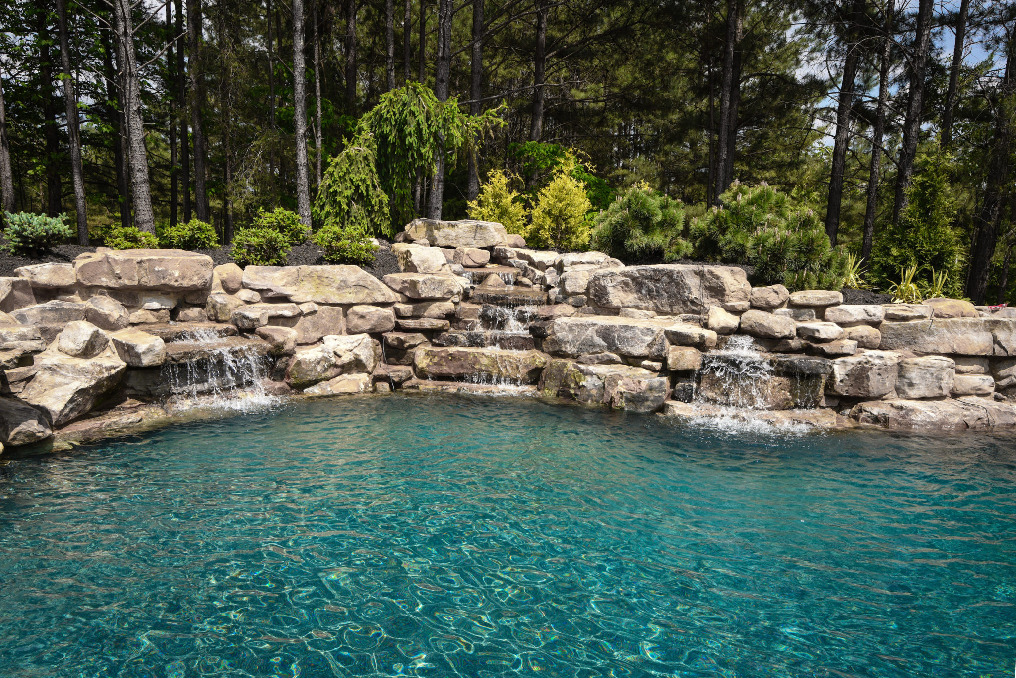 A custom boulder wall with multiple sheer descent water features cascading into a swimming pool.