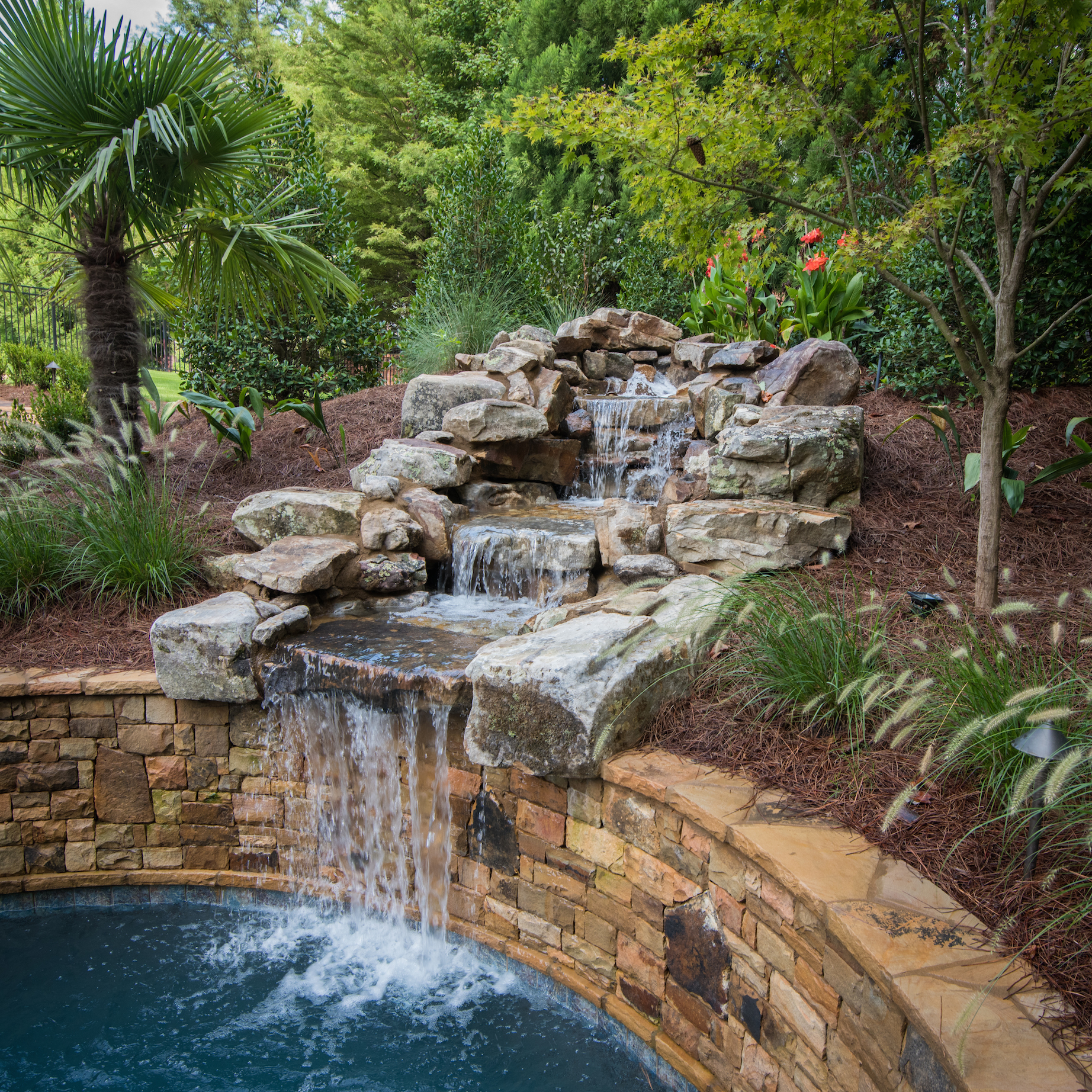 A three-tier boulder waterfall flowing into a swimming pool.