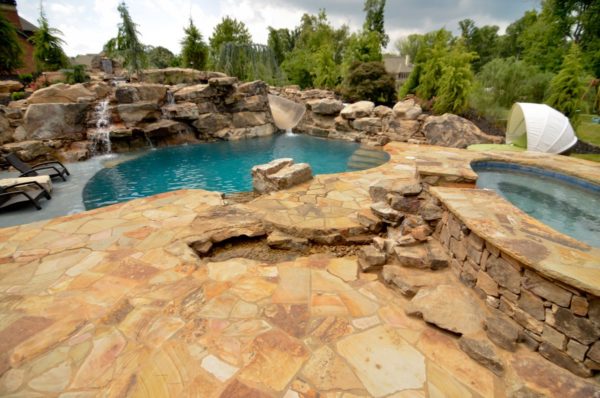 A custom freeform pool surrounded by lush greenery, with a boulder waterfall and slide.