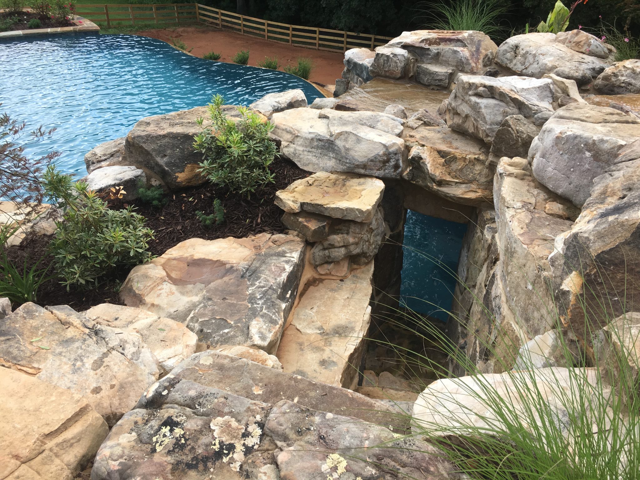 A custom boulder wall with a grotto and private side entrance beside a swimming pool.