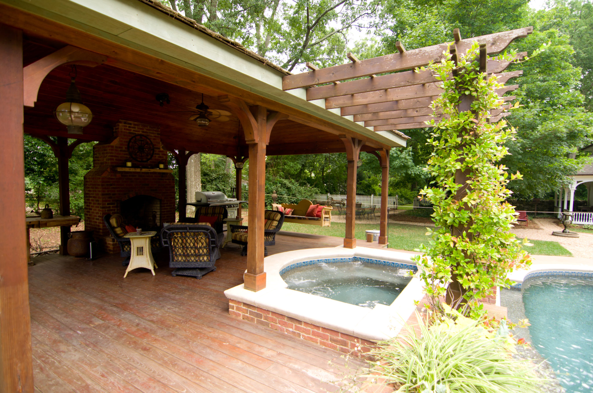 A picturesque wood vaulted cabana with pergola and fireplace next to a swimming pool.