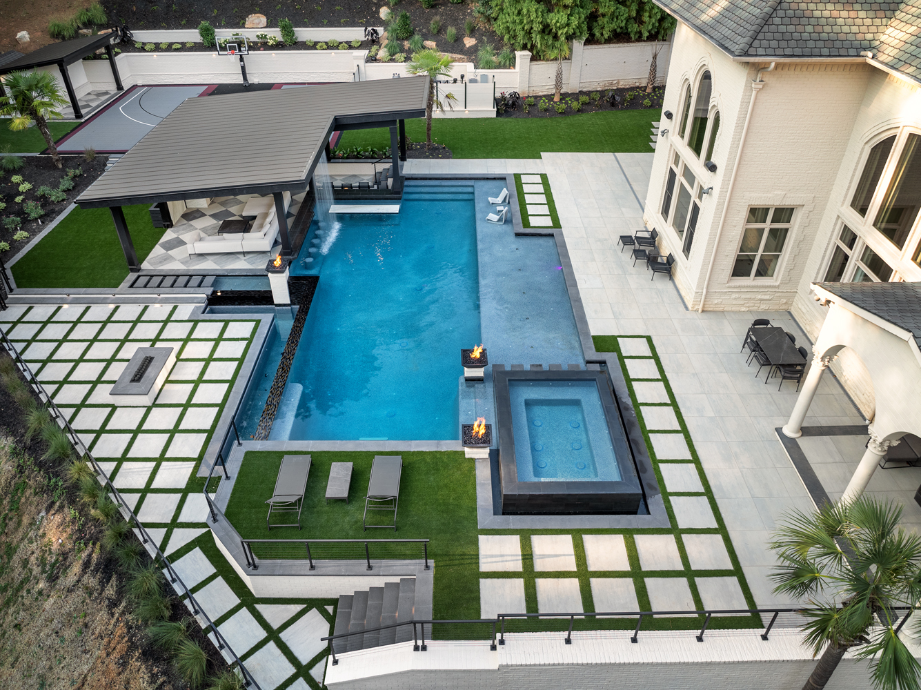 Aerial view of Grady Jarrett's modern luxury backyard, featuring a large pool, 360-degree infinity spa, fire bowls, cabana with rain curtain, outdoor kitchen, and sports court, designed by Georgia Classic Pool.