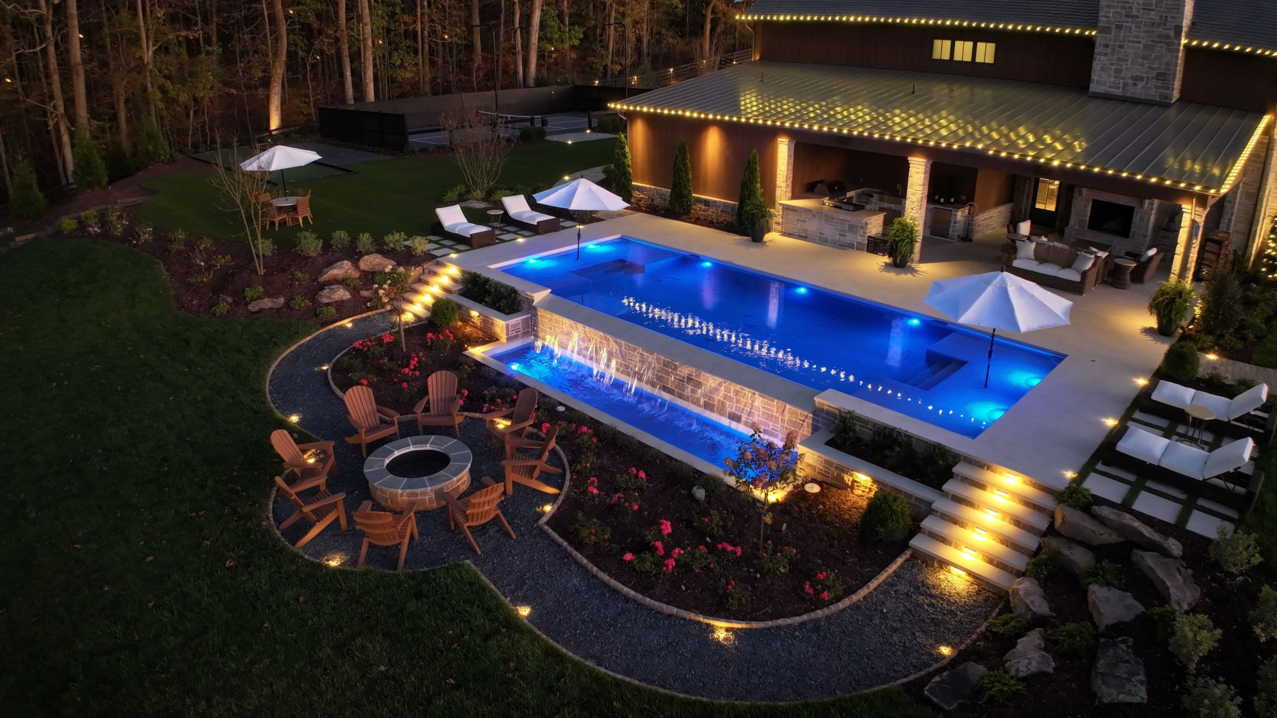 Modern farmhouse swimming pool with a sleek rectangular design, vanishing edge overflow, travertine deck, and clean landscaping.