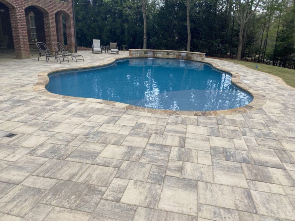 Freeform pool with paver deck, stone coping, and a raised stone wall with sheer descent water features